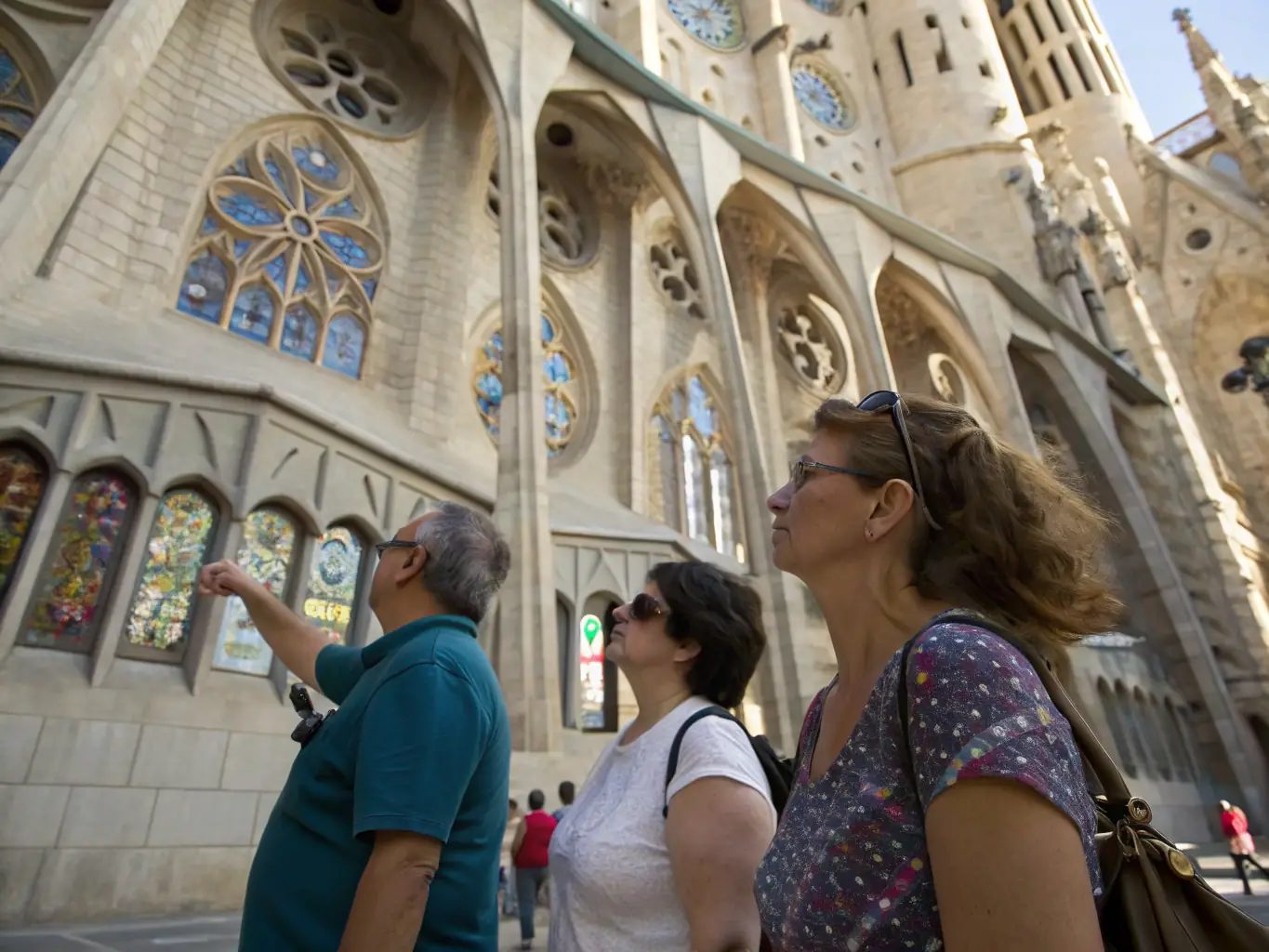 A group of visitors listening attentively to a guide in front of the cathedral, with detailed architecture visible in the background. The guide is pointing to a specific architectural detail, and the visitors are looking up with interest.